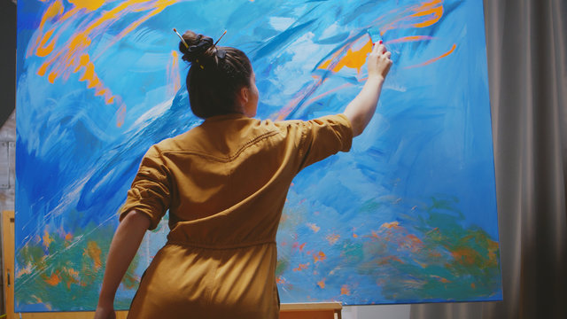 Innovative female painter using orange paint on big canvas.