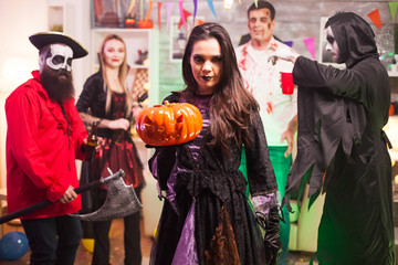 Witch holding a pumpkin and looking at the camera while celebrating halloween.