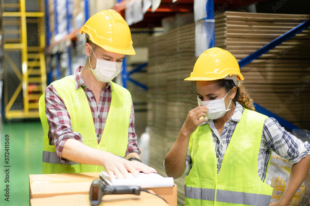 Wall mural Warehouse workers wearing face mask to protect for pollution and virus discussing with clip board in the warehouse.