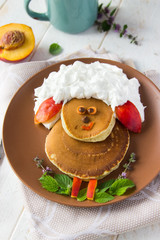Obraz premium Creative idea for a kids breakfast, sheep, ram made from pancakes, whipped cream, fruit. food art idea. Children, holidays, summer,Easter, healthy, proper nutrition concept. Free space for text. Baby 