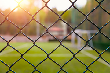 Fototapeta premium Astroturf or synthetic grass soccer field with blurred white lines and goal post behind the metal fence