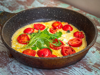 Hot breakfast in a pan with eggs and tomatoes on a variegated background