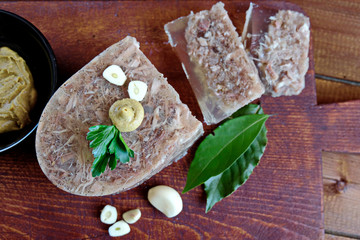  Home jelly, cut into portions lying on the kitchen Board.Near mustard, garlic, Bay leaf, parsley. Place for text. Top view.