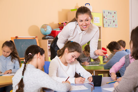Smiling woman teacher helping to group of children at drawing lesson at class