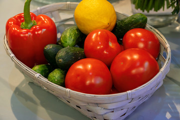 Vegetables in a basket next to bunches of herbs on the kitchen table.