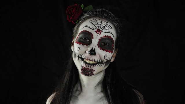 Mexican day of the dead. Young woman with sugar skull Halloween makeup looking at the camera and smiling. Extreme close-up. Happy Halloween.