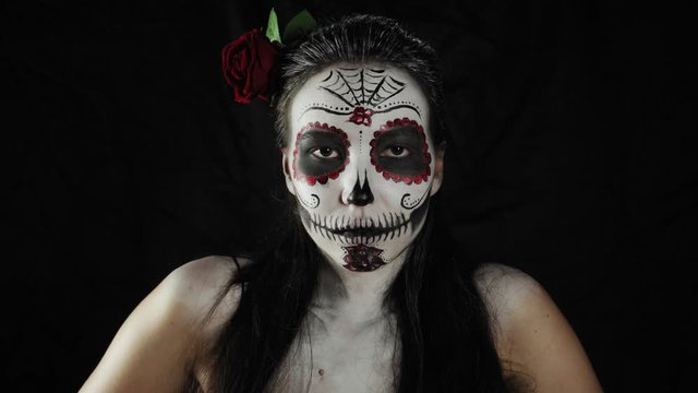 Mexican day of the dead. Young woman with sugar skull Halloween makeup looking at the camera and smiling. Extreme close-up. Happy Halloween.