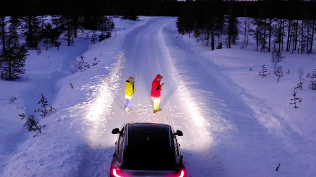 Aerial view, couple of young people are dancing in front of car during winter trip to northern country. Carefree friends enjoy life having fun with each other
