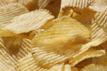 Background corrugated golden chips with texture. Potato chips is snack, ready to eat and fat food or junk food. Horizontal. Top view.