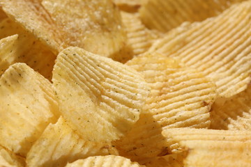Background corrugated golden chips with texture. Potato chips is snack, ready to eat and fat food or junk food. Horizontal. Top view.