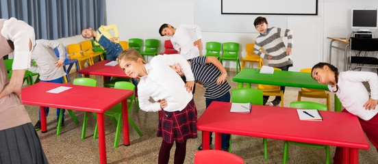 Portrait of children stretching with friendly female teacher during physical activity break in school