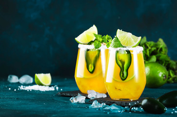 Spicy margarita cocktail with tequila, mango juice, jalapeno pepper, lime and salt, blue background, copy space - obrazy, fototapety, plakaty