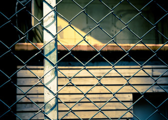 Closeup of metal net with a wooden house behind it. Toned image.