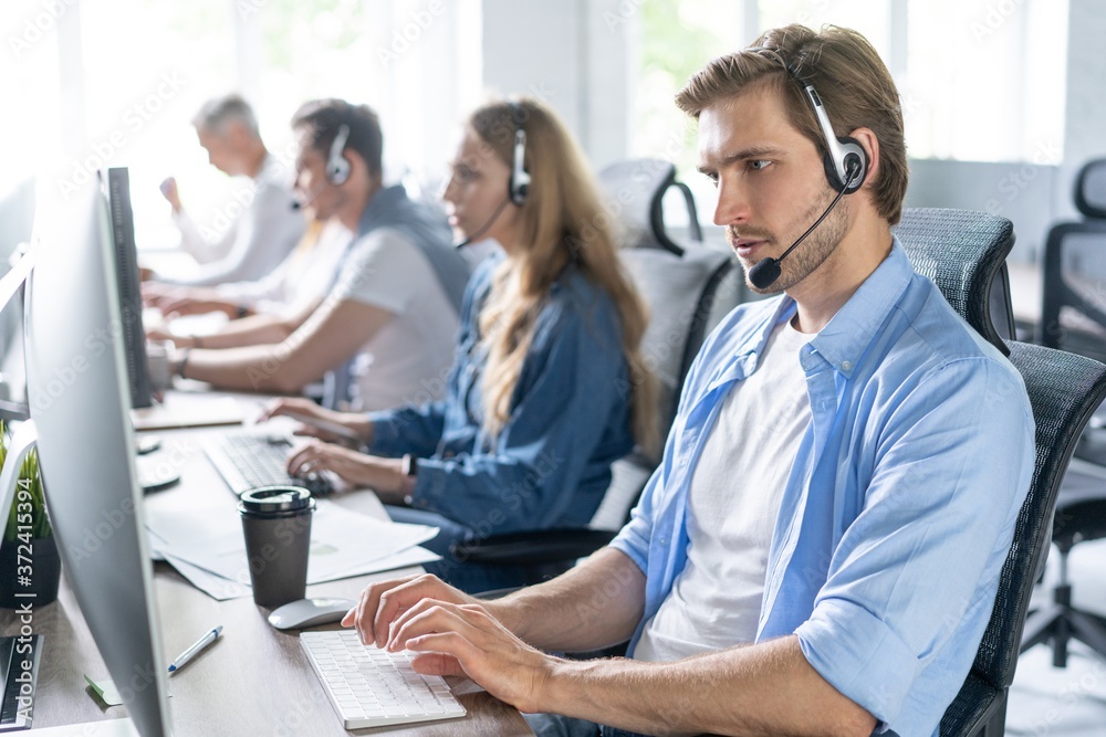 Wall mural young handsome male customer support phone operator with headset working in call center.