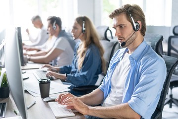 Young handsome male customer support phone operator with headset working in call center. - obrazy, fototapety, plakaty