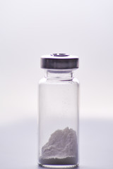 Obraz na płótnie Canvas a small glass vial contains an unknown white substance, could be cocaine, heroine, pcp, meth, salt or sugar, you decide