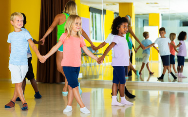 Group of kids with their teacher holding hands and dancing in circle in dance school