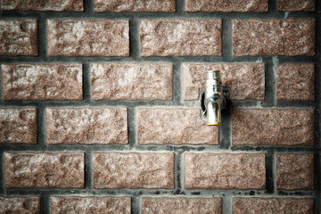 A faucet on a red brick wall. Toned image. Vignetting effect.