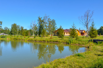 Obraz premium wooden house made of beams and boards in a Russian village, field, pond and blue sky