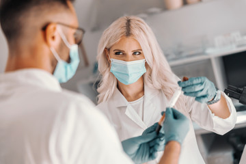 Two dedicated medical workers standing in laboratory and holding test tube with blood sample.