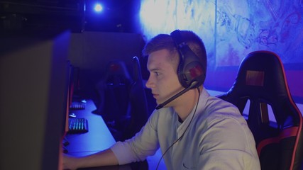 Young man spending time in modern e-sport club playing shooter video game
