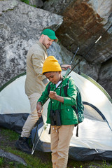 African little boy helping to his father setting up the tent outdoors during their camping