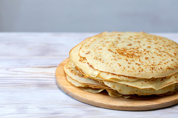 fried pancakes are stacked on wooden plate on kitchen table.
