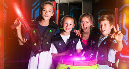 Fototapeta premium Group portrait of happy teenagers with laser guns having fun on dark lasertag arena..
