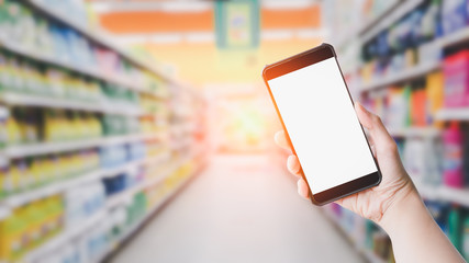 Shopping online concept. Hand holding black smartphone and white blank screen in blurry at shopping or department store background. Mock up shopping.