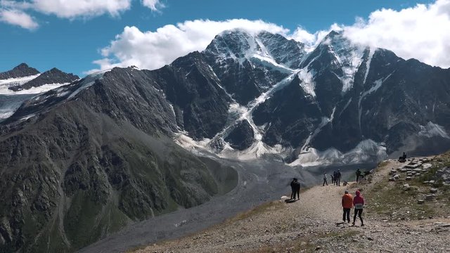 Dongusorun and Nakra-tau from Pik Cheget. Hikers on a sunny summer day on the top of Mount Cheget, against the backdrop of a huge mountain snowy peak and the "Seven" glacier. Great Caucasian ridge.