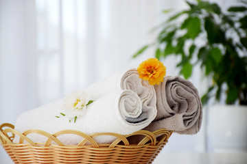 Fototapeta na wymiar Fresh gray and white towels rolled in wicker bascket decorated with flowers and liquid container. Spa and wellness, massage or beauty salon, laundry or dry-cleaning concept.