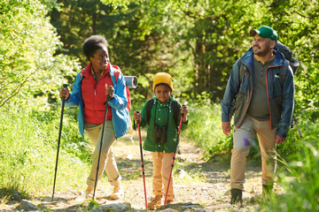 Multiethnic family of three walking in the forest together the go hiking