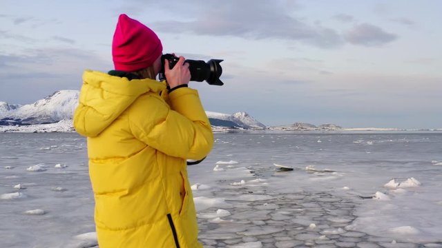 Aerial view from drone of female photographer in yellow jacket discovering Nordic nature during travel, hipster girl blogger wanderlust with camera taking photo of scenery winter landscape in journey
