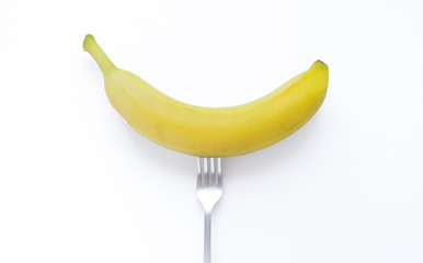 A yellow banana on a fork. fresh juisy raw fruit yellow banana on the fork. Vegetarian and vegan concept. Organic Vegan Healthy Shop or Store.