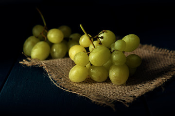 Close-up part of grape cluster on the burlap napkin and dark wooden table.