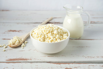 Bowl with cottage cheese and jug of milk on white Provence style wooden table