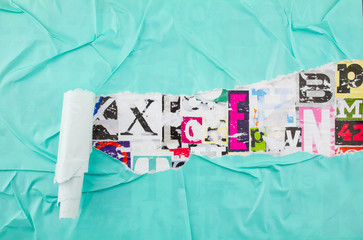 Torn and peeling azure blue paper poster on colorful collage from clippings with letters and...