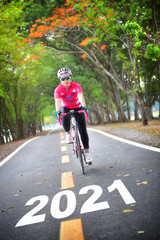 Fototapeta na wymiar Road to new year 2021, Sportswoman ride bike on countryside with tree tunnel, healthy lifestyle concept and keep moving idea