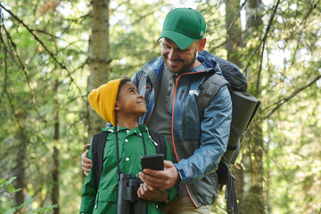 Smiling father showing something to his son on mobile phone during their hiking in the forest
