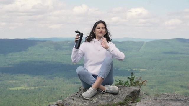 A girl is resting on the top of a mountain after a hike and drinking hot tea