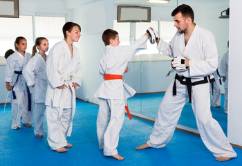 Fototapeta na wymiar Young children are practicing on boxing paws with coach during karate class.