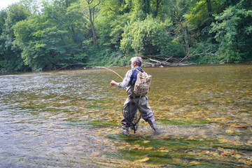Man fly fishing in the summer in a beautiful river with clear water