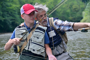 A father and his son fly fishing in summer on a beautiful trout river with clear water