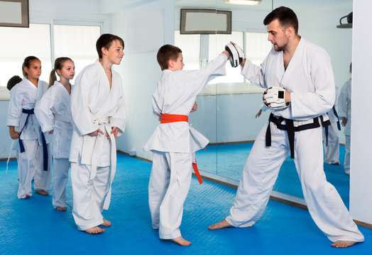 Young children are practicing on boxing paws with coach during karate class.