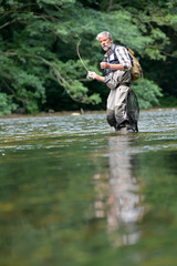 Man fly fishing in the summer in a beautiful river with clear water