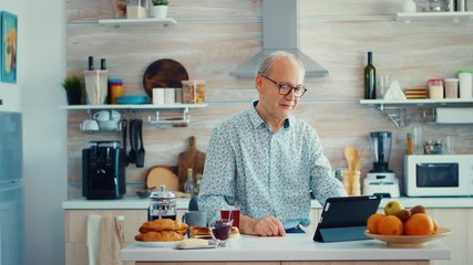 Happy senior man during breakfast in kitchen having a video conference with family. Elderly person using internet online chat technology video webcam making a video call connection camera - Powered by Adobe