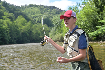 young boy fly fishing in summer in a beautiful river with clear water