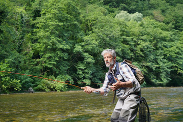 Man fly fishing in the summer in a beautiful river with clear water