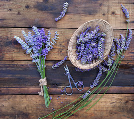 bunch of lavender flowers next to a little basket full of petals  with scisors on wooden background