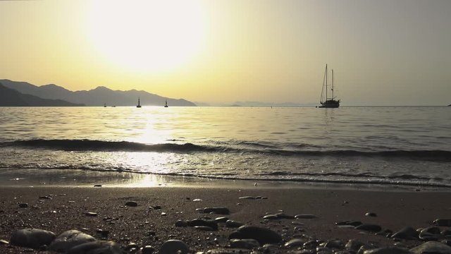 Yacht at anchor as waves lap on sandy beach in the golden morning sun